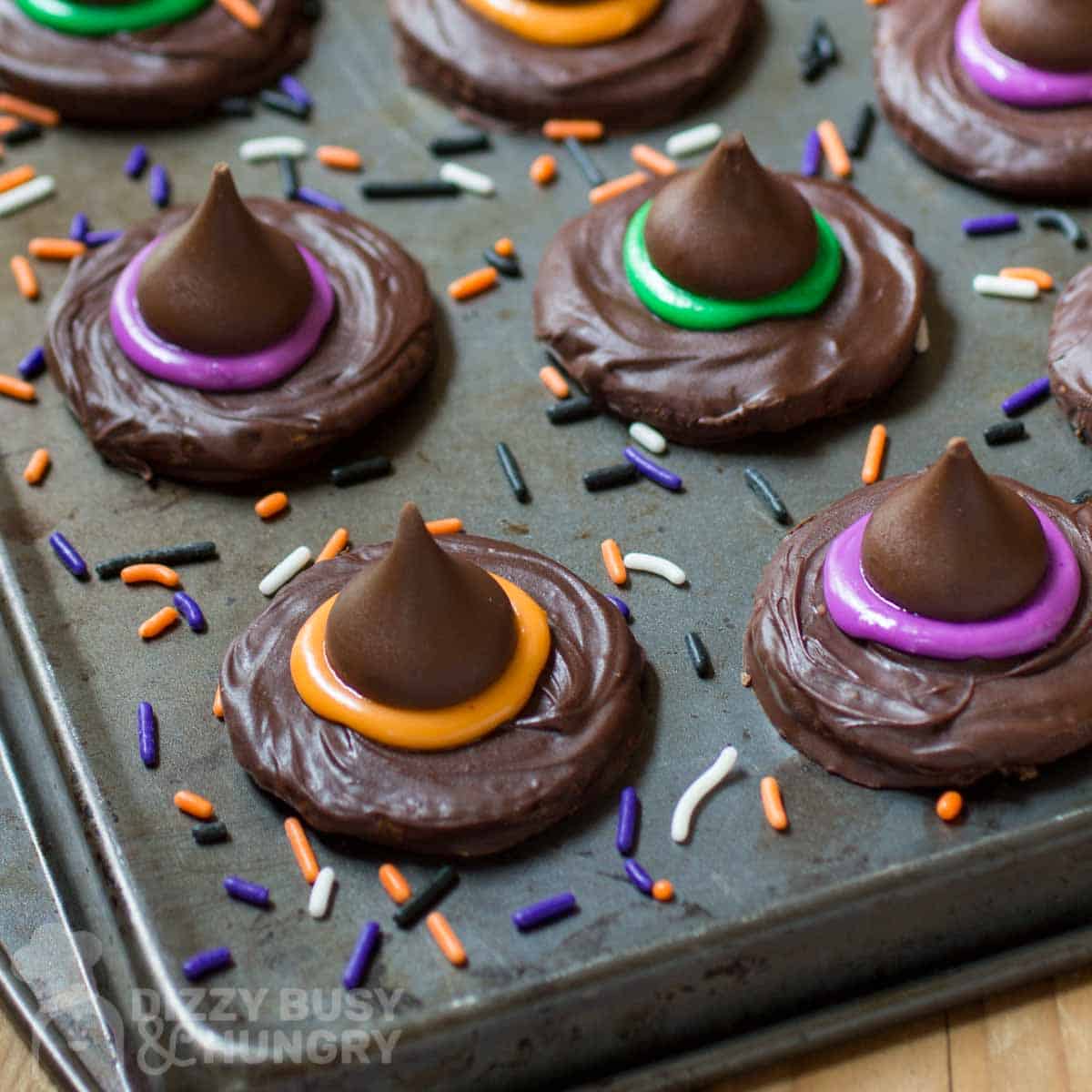 Side shot of witch hat cookies on a baking sheet with halloween sprinkles scattered around.