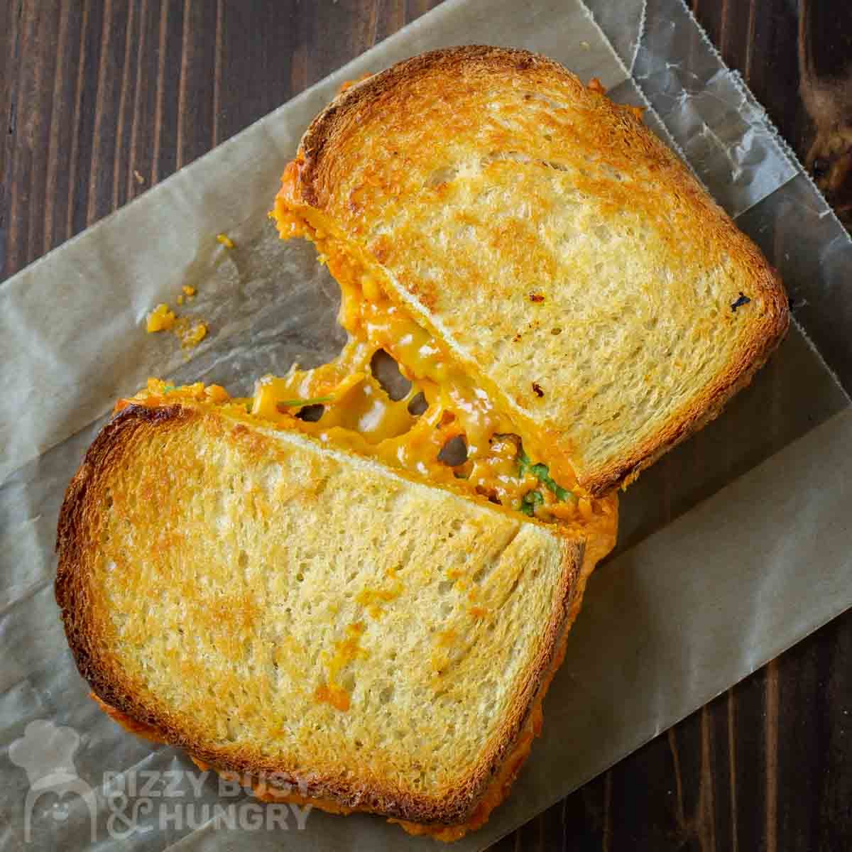Overhead shot of a pumpkin grilled cheese split in half with cheese pulled in the middle on a piece of wax paper.