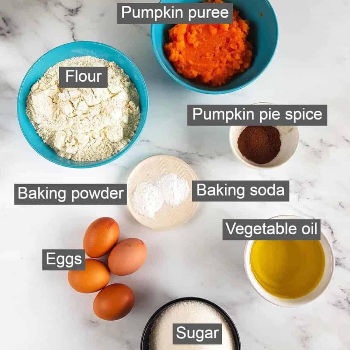 Overhead shot of ingredients - pumpkin puree, flour, pumpkin pie spice, baking powder, baking soda, vegetable oil, eggs, and sugar.