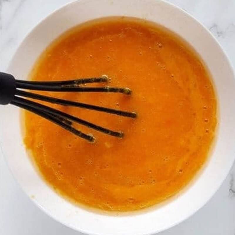 Overhead view of process shot 2 - in a second bowl, combine the vegetable oil, eggs, sugar, and pumpkin puree. Whisk until the ingredients are just combined.