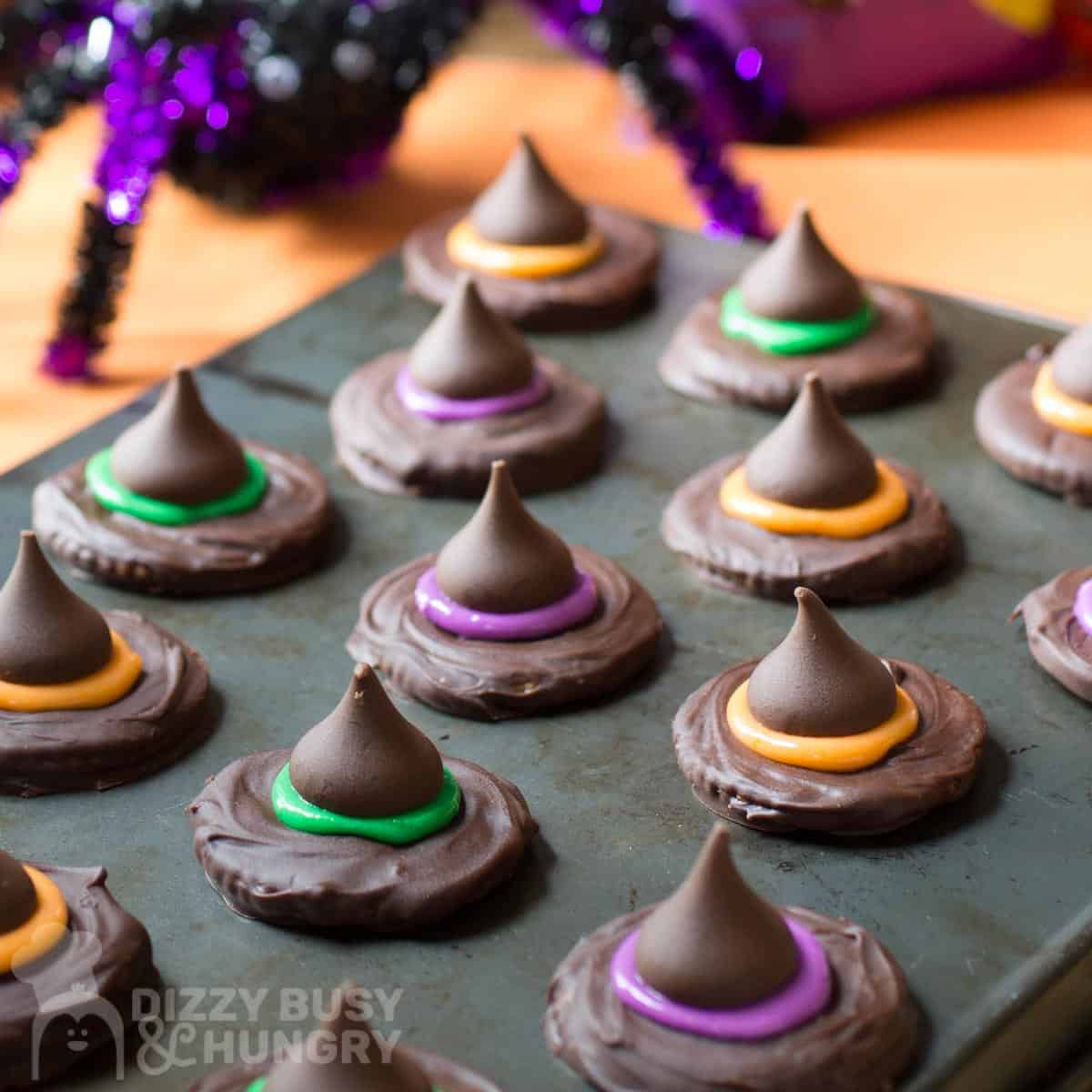 Side shot of witch hat cookies on a baking sheet with a spider decoration in the background.