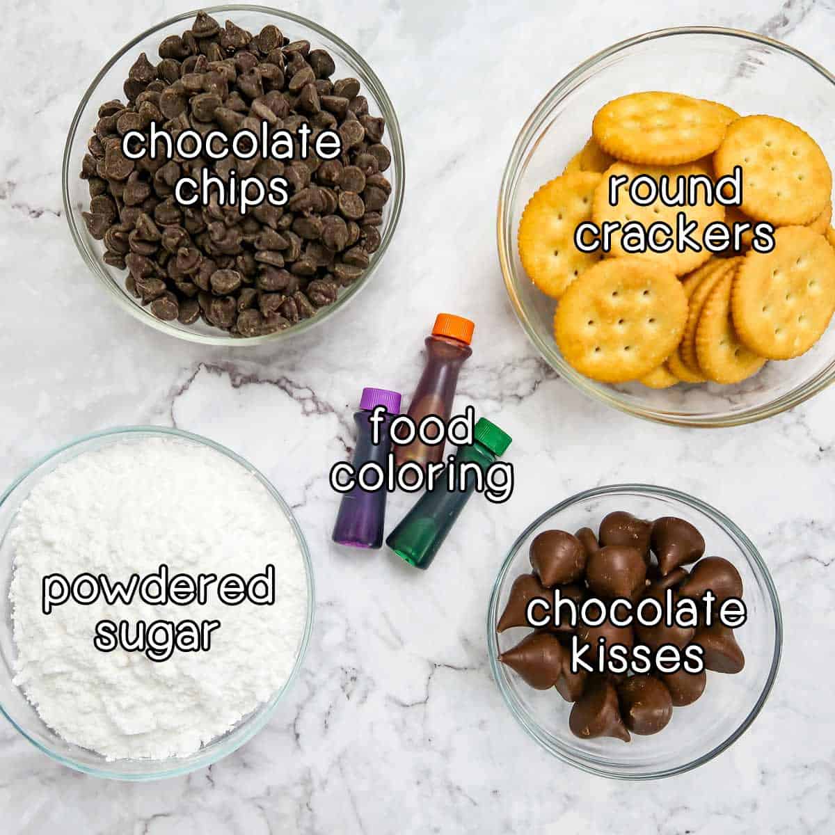 Overhead shot of ingredients - chocolate chips, round crackers, food coloring, chocolate kisses, and powdered sugar.
