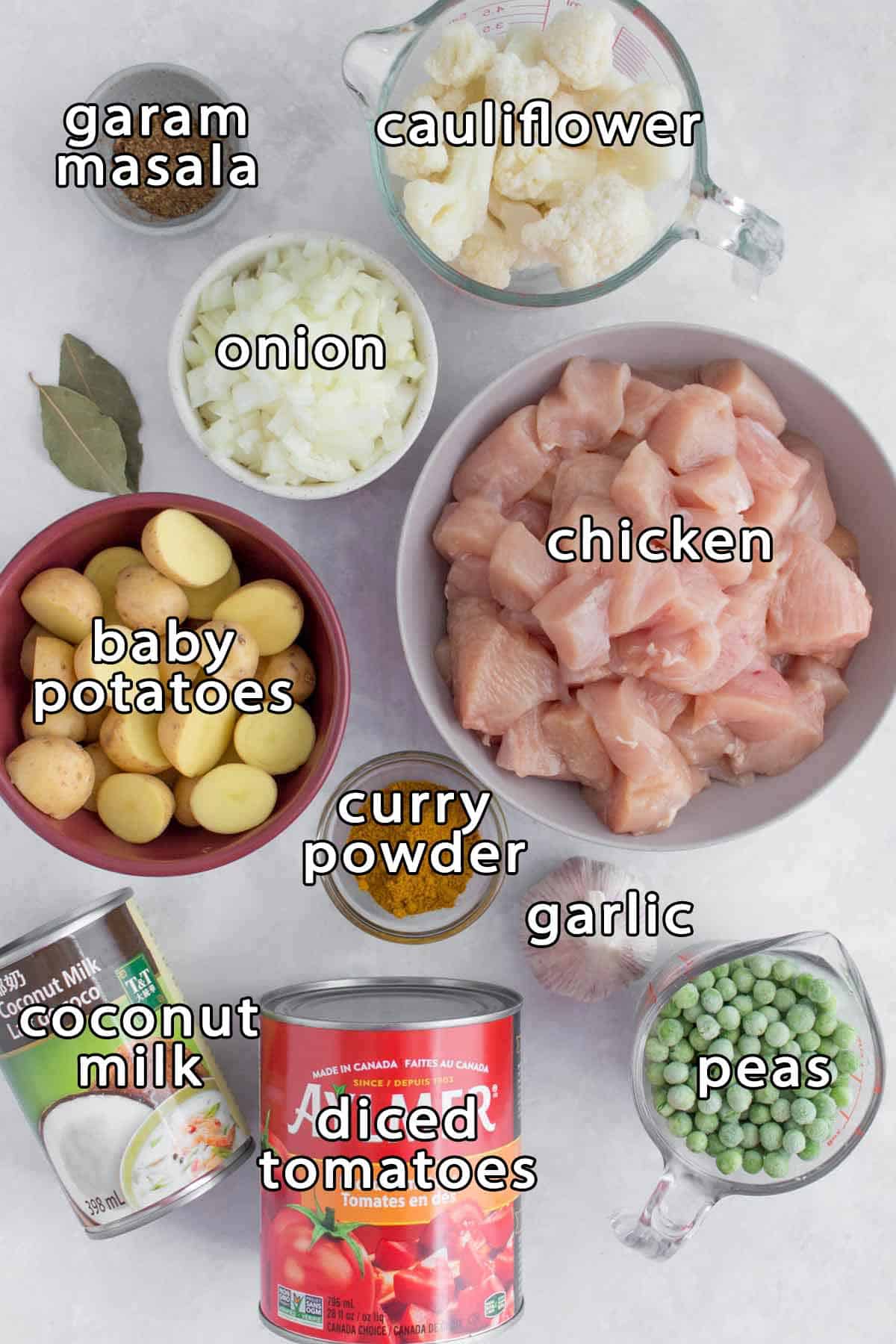 Overhead shot of ingredients - garam masala, cauliflower, onion, bay leaves, baby potatoes, chicken, curry powder, garlic, peas, diced tomatoes, and coconut milk.
