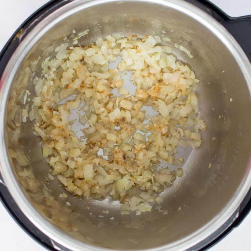 Overhead view of process shot 1 - on saute mode in your instant pot, add the olive oil and diced onions. Saute for a minute before adding the minced garlic and saute for another minute.