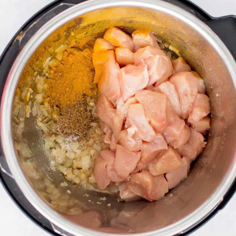 Overhead view of process shot 2 - while still on saute mode, quickly add in the diced chicken, curry powder, garam masala, and salt.