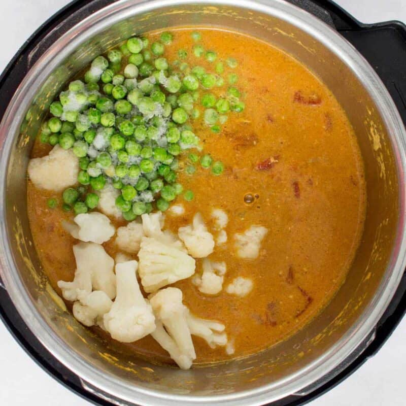 Overhead view of process shot 6 - remove the bay leaves. Add in the frozen cauliflower and frozen peas.