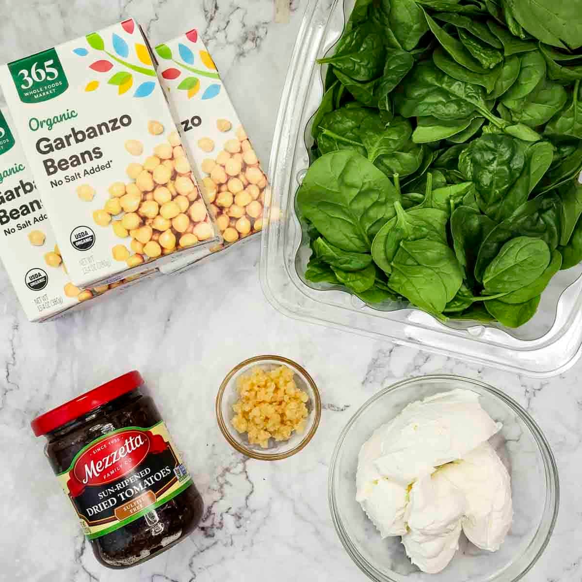 Overhead shot of ingredients - chickpeas, spinach, sun-dried tomatoes, minced garlic, and cream cheese.
