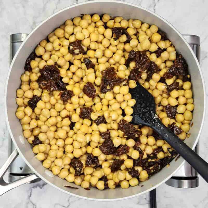 Overhead view of process shot 2 - add the chickpeas and ¼ cup of water intot he skillet. Season with salt and pepper and cook for 5 minutes until the chickpeas are heated through.