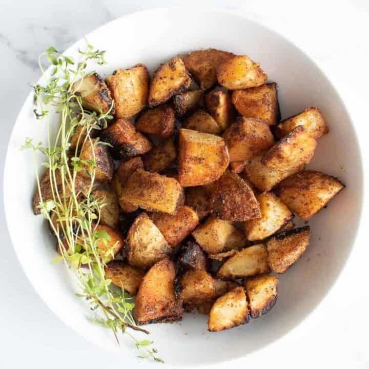 Overhead shot of golden brown potatoes in a white bowl with a bundle of greens on the side.