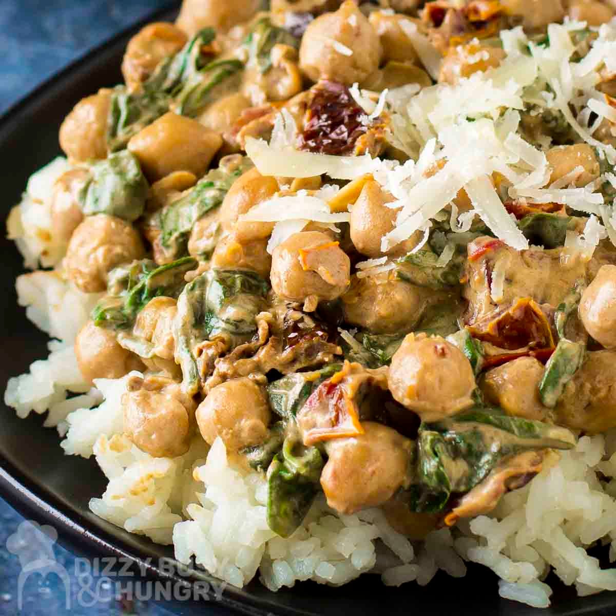 Close up shot of marry me chickpeas and spinach on a bed of rice garnished with shaved parmesan on a black plate.