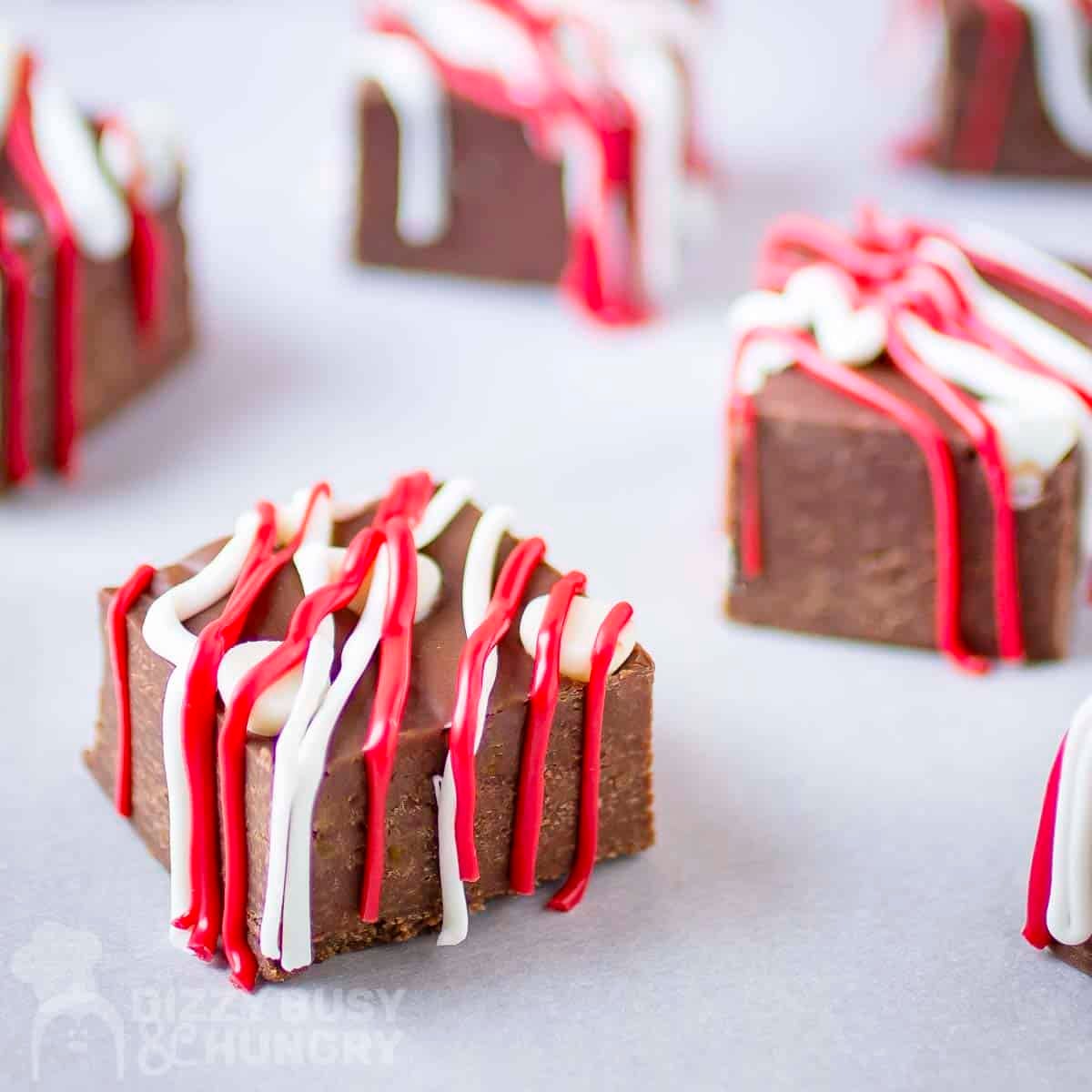 Side shot of multiple pieces of fudge drizzled with red and white melted chocolate on a white surface.